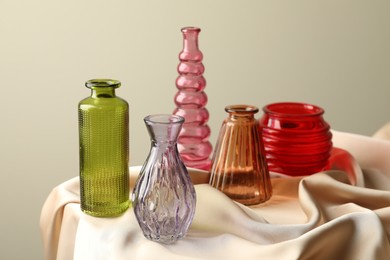 Photo of Different beautiful glass vases on beige cloth against light background, closeup