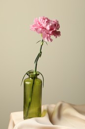 Photo of Beautiful flower in glass vase on beige cloth against light background