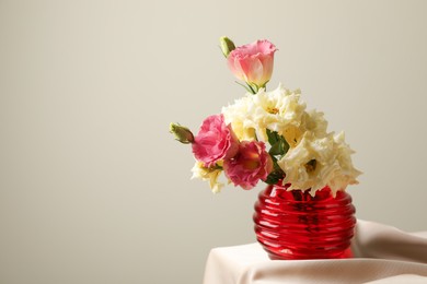Photo of Beautiful flowers in glass vase on beige cloth against light background, space for text