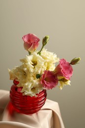 Photo of Beautiful flowers in glass vase on beige cloth against light background, closeup