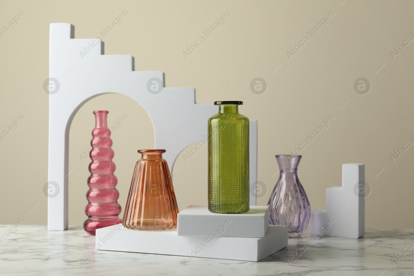 Different beautiful glass vases on white marble table against beige background Photo of Different beautiful glass vases on white marble table against beige background