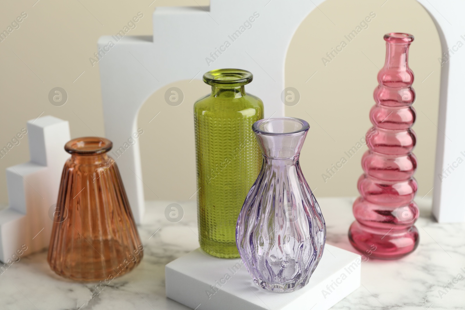 Different beautiful glass vases on white marble table against beige background, closeup Photo of Different beautiful glass vases on white marble table against beige background, closeup