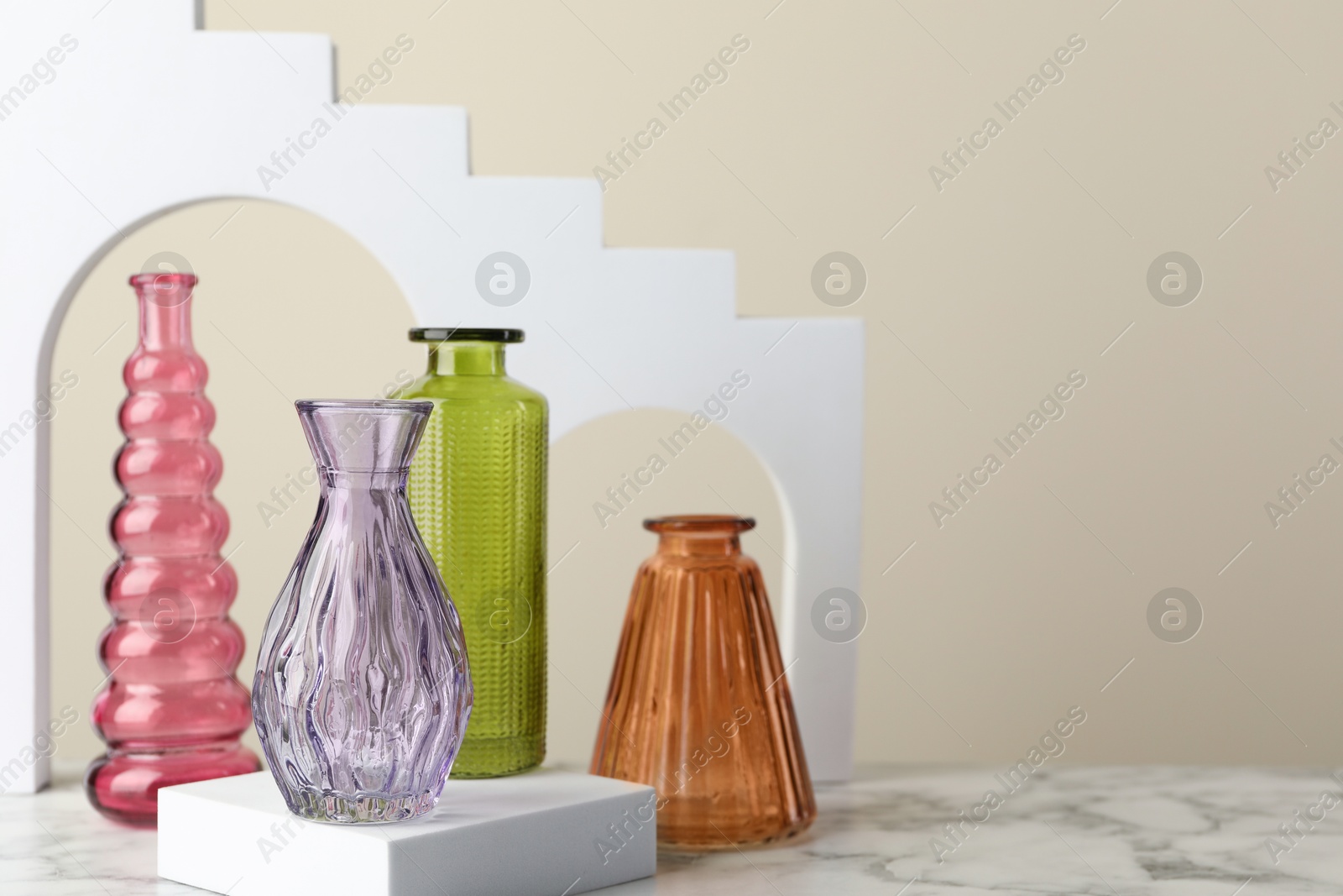 Different beautiful glass vases on white marble table against beige background, closeup. Space for text Photo of Different beautiful glass vases on white marble table against beige background, closeup. Space for text