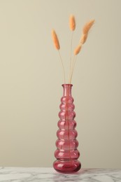 Photo of Dry spikes in glass vase on white marble table against beige background