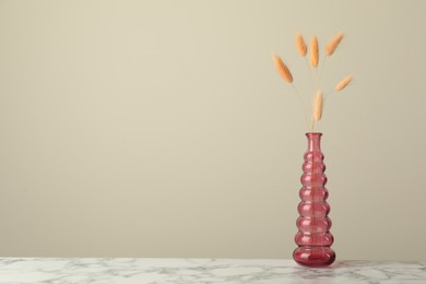 Photo of Dry spikes in glass vase on white marble table against beige background, space for text
