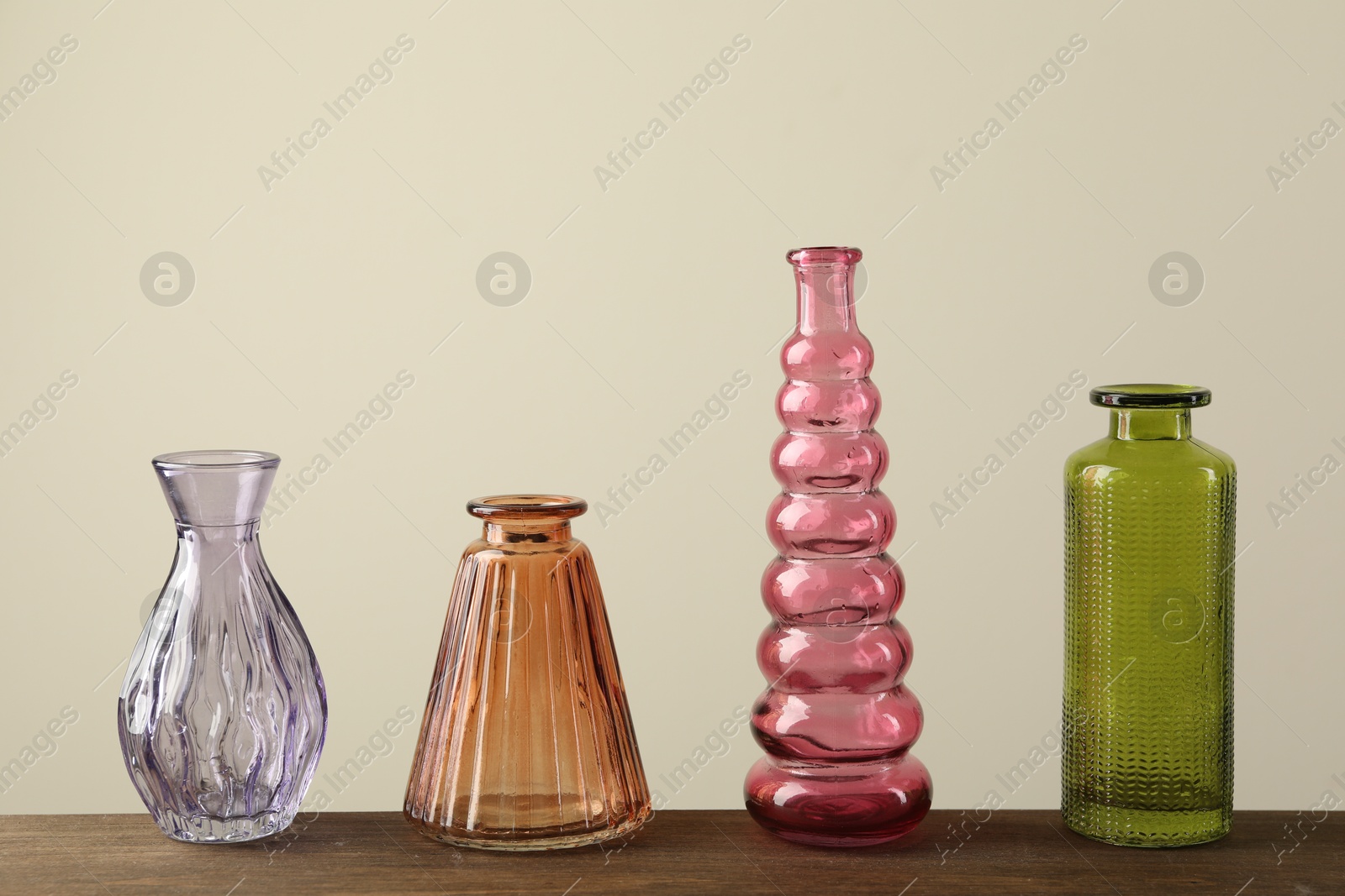 Different beautiful glass vases on wooden table against beige background Photo of Different beautiful glass vases on wooden table against beige background