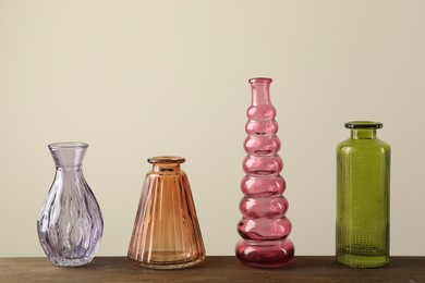 Photo of Different beautiful glass vases on wooden table against beige background
