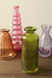 Photo of Different beautiful glass vases on wooden table against beige background, closeup