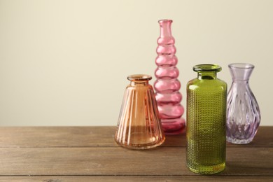 Photo of Different beautiful glass vases on wooden table against beige background, closeup. Space for text