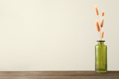 Photo of Dry spikes in glass vase on wooden table against beige background, space for text
