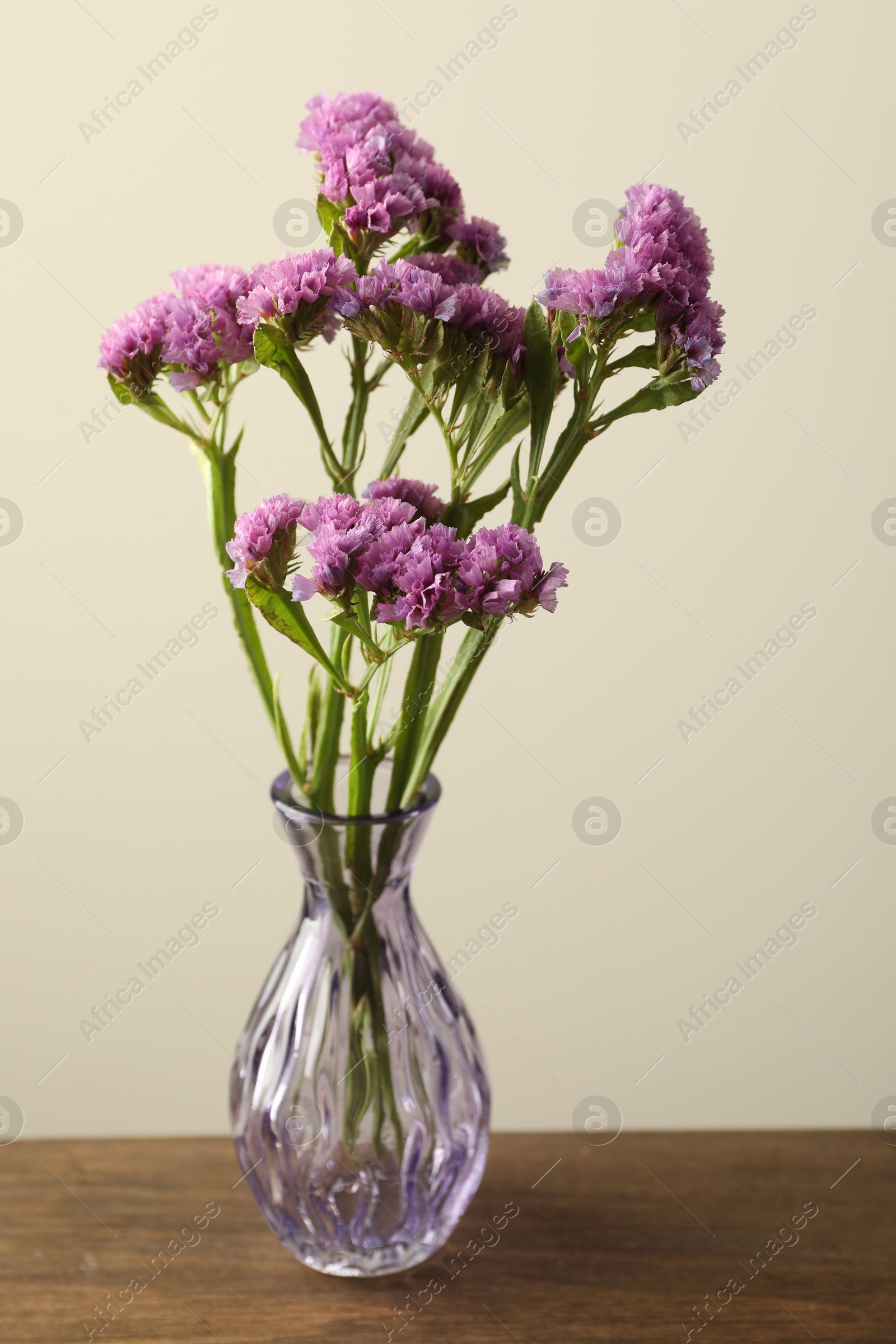 Beautiful flowers in glass vase on wooden table against beige background, closeup Photo of Beautiful flowers in glass vase on wooden table against beige background, closeup