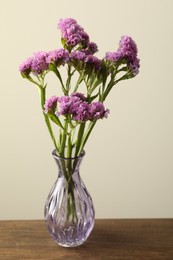 Photo of Beautiful flowers in glass vase on wooden table against beige background, closeup