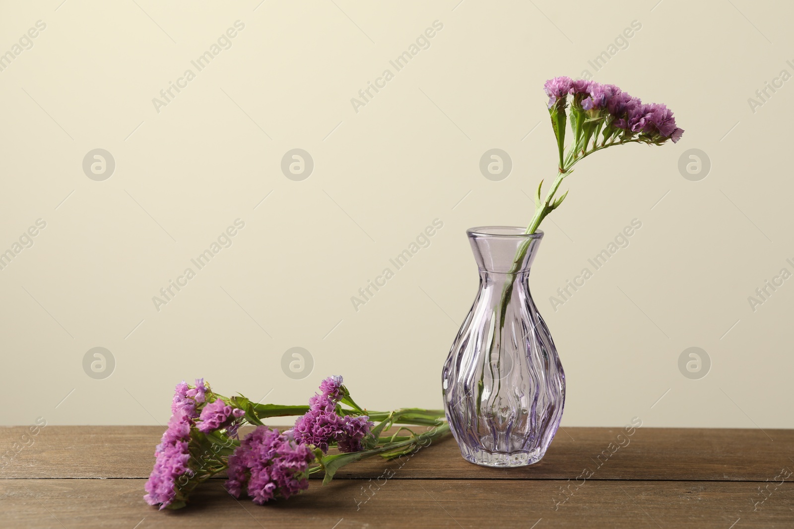Beautiful flowers and glass vases on wooden table against beige background Photo of Beautiful flowers and glass vases on wooden table against beige background