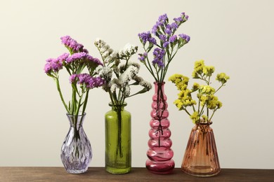 Photo of Beautiful flowers in glass vases on wooden table against beige background