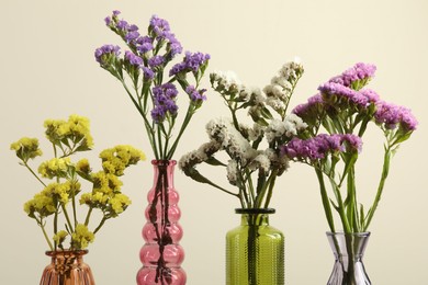 Photo of Beautiful flowers in glass vases against beige background, closeup