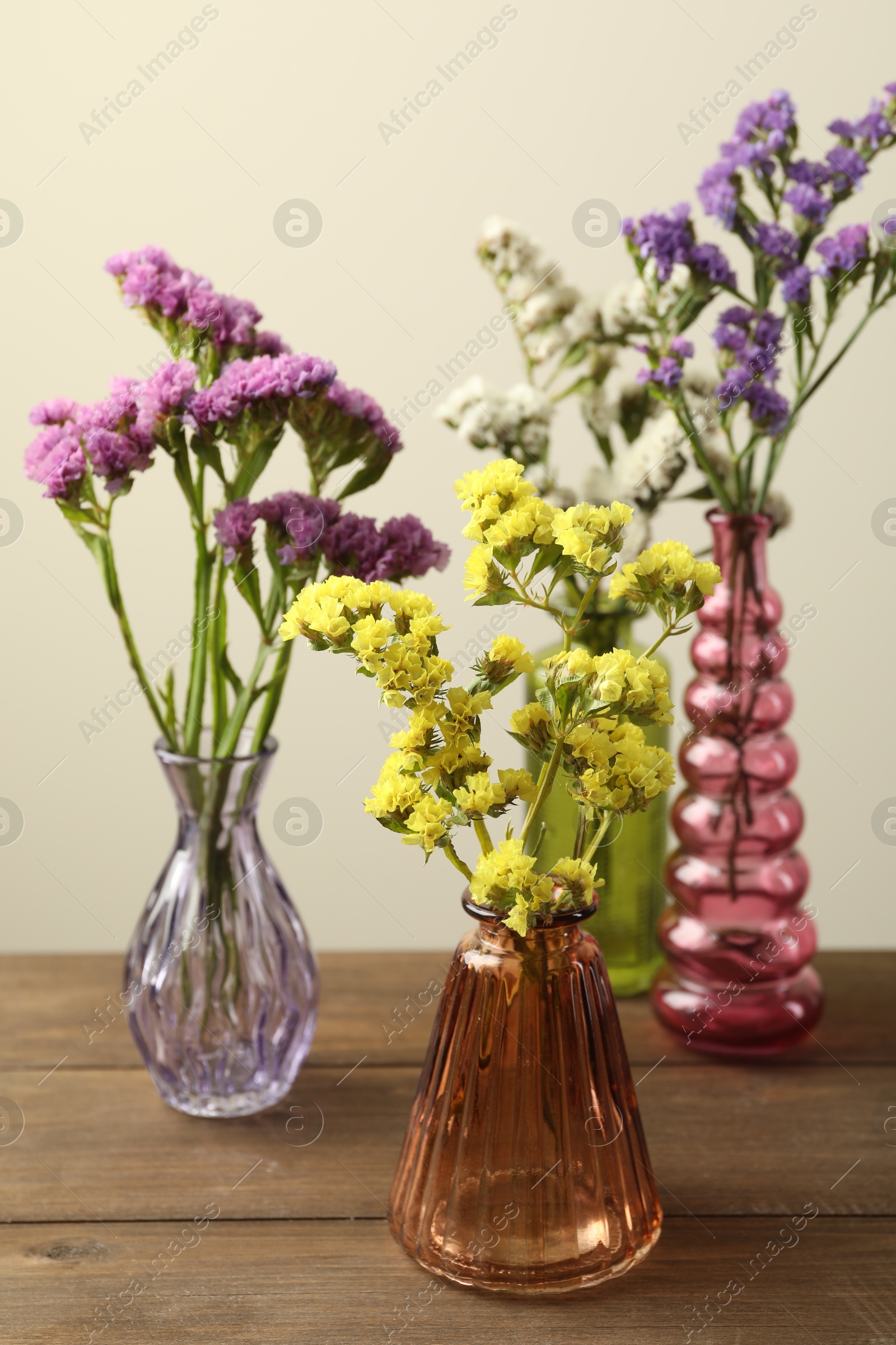 Beautiful flowers in glass vases on wooden table against beige background, closeup Photo of Beautiful flowers in glass vases on wooden table against beige background, closeup