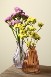 Photo of Beautiful flowers in glass vases on wooden table against beige background, closeup