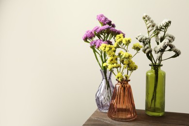 Photo of Beautiful flowers in glass vases on wooden table against beige background, space for text
