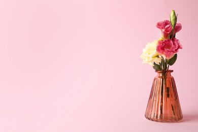 Photo of Beautiful flowers in glass vase on pink background, space for text