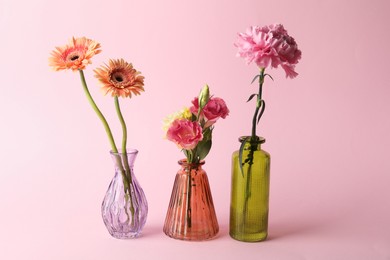 Photo of Beautiful flowers in glass vases on pink background