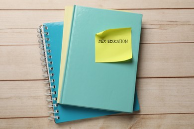 Photo of Sticky note with words Sex Education and notebooks on wooden table, top view