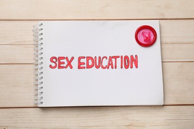 Photo of Notebook with words Sex Education and condom on wooden table, top view