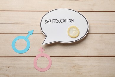Photo of Paper speech bubble with words Sex Education, gender symbols and condom on wooden table, flat lay