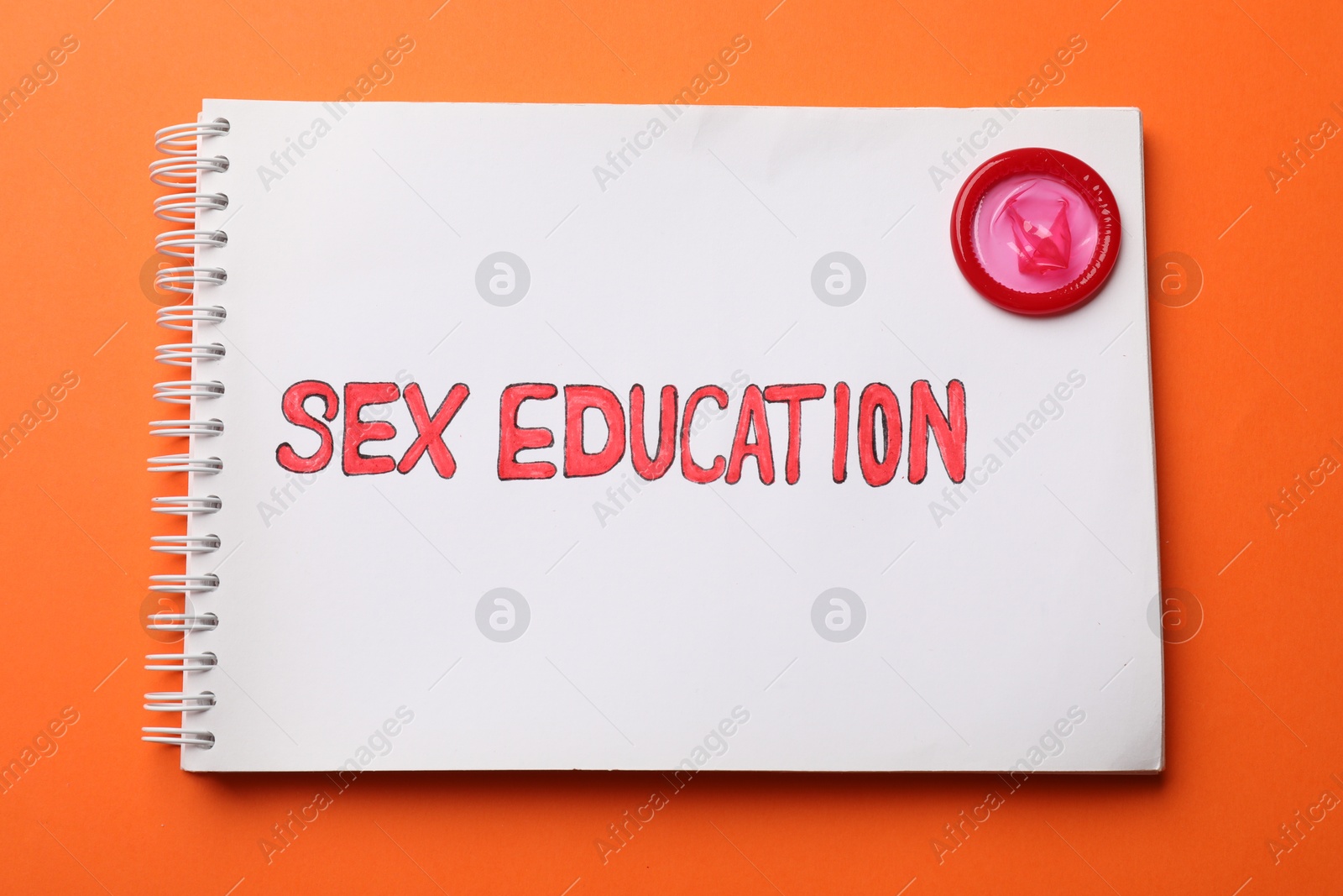 Photo of Notebook with words Sex Education and condom on orange background, top view