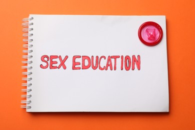 Photo of Notebook with words Sex Education and condom on orange background, top view