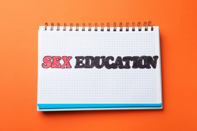 Photo of Notebook with words Sex Education on orange background, top view