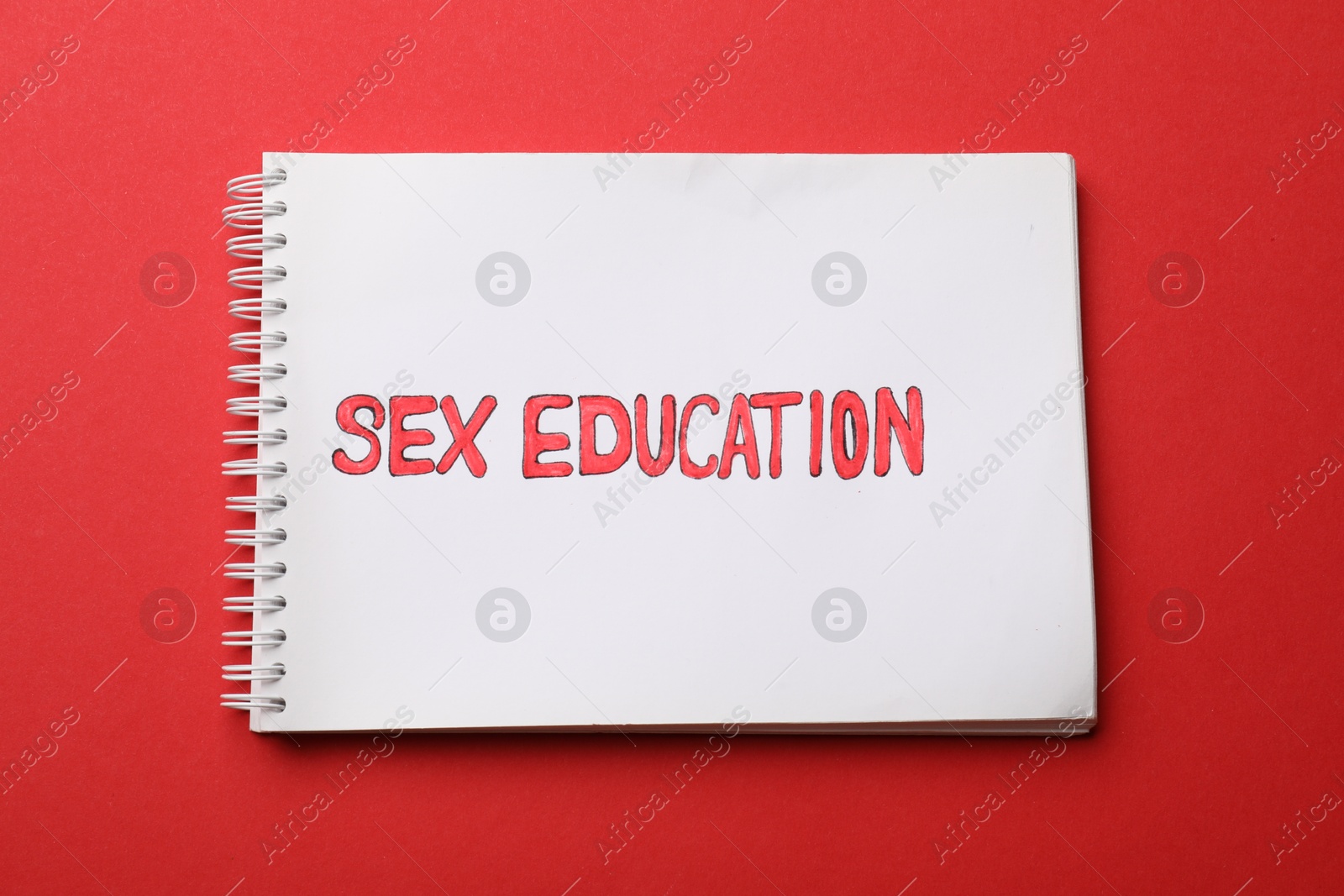 Photo of Notebook with words Sex Education on red background, top view