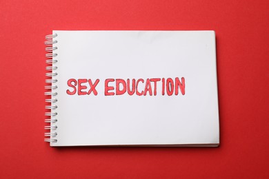 Photo of Notebook with words Sex Education on red background, top view