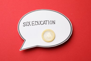 Photo of Paper speech bubble with words Sex Education and condom on red background, top view