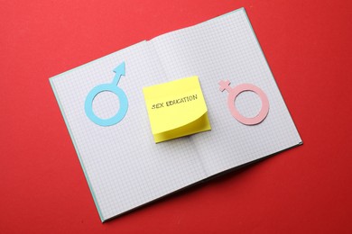Photo of Sticky note with words Sex Education, gender symbols and notebook on red background, top view
