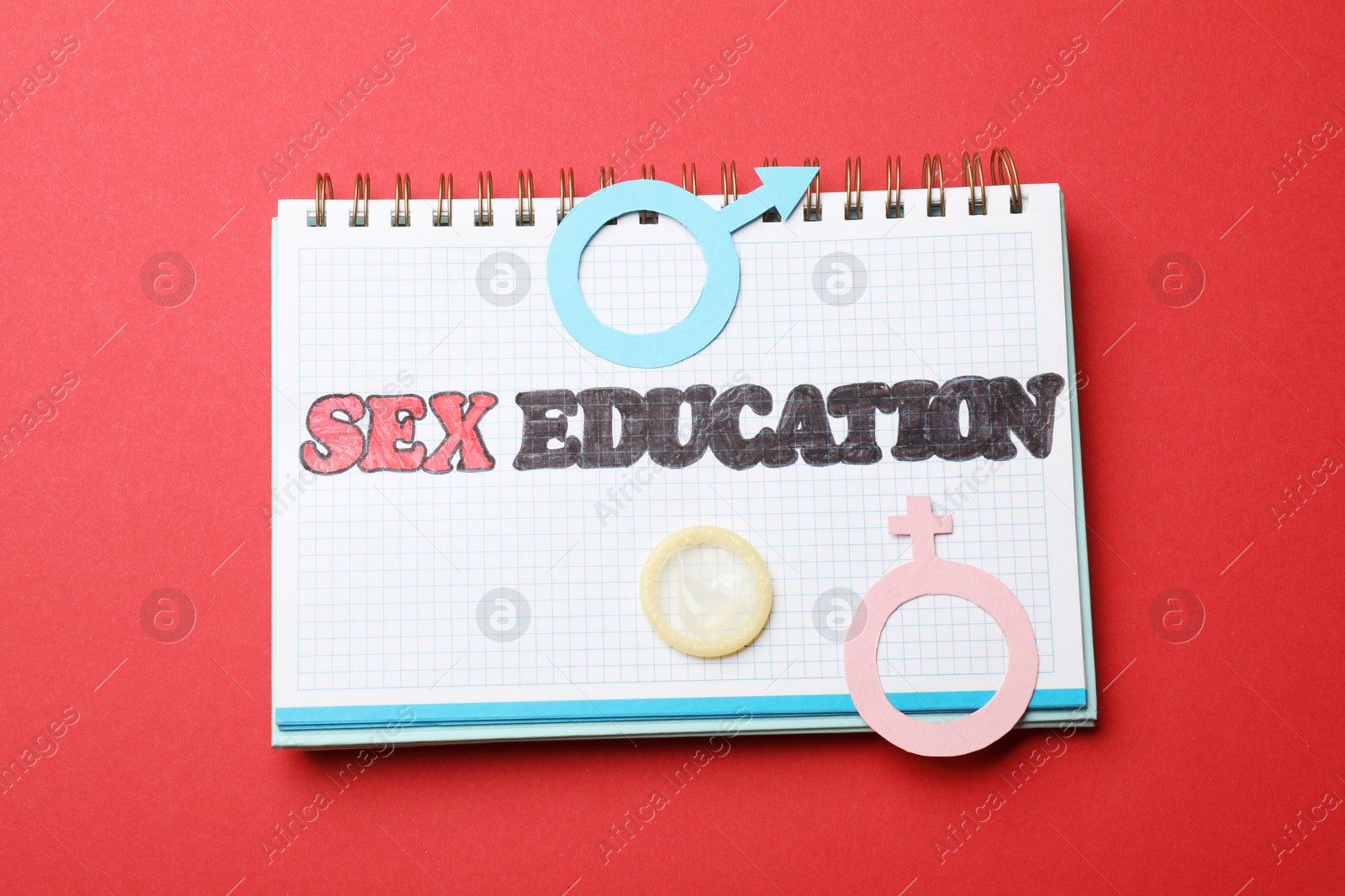 Photo of Notebook with words Sex Education, gender symbols and condom on red background, top view