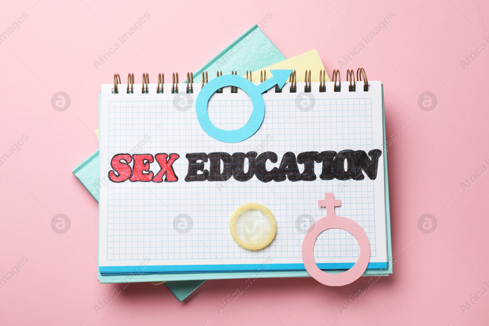 Photo of Notebook with words Sex Education, gender symbols and condom on pink background, top view