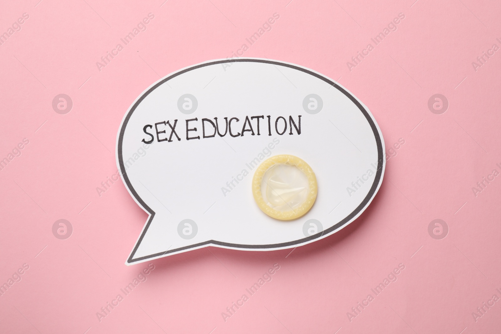 Photo of Paper speech bubble with words Sex Education and condom on pink background, top view