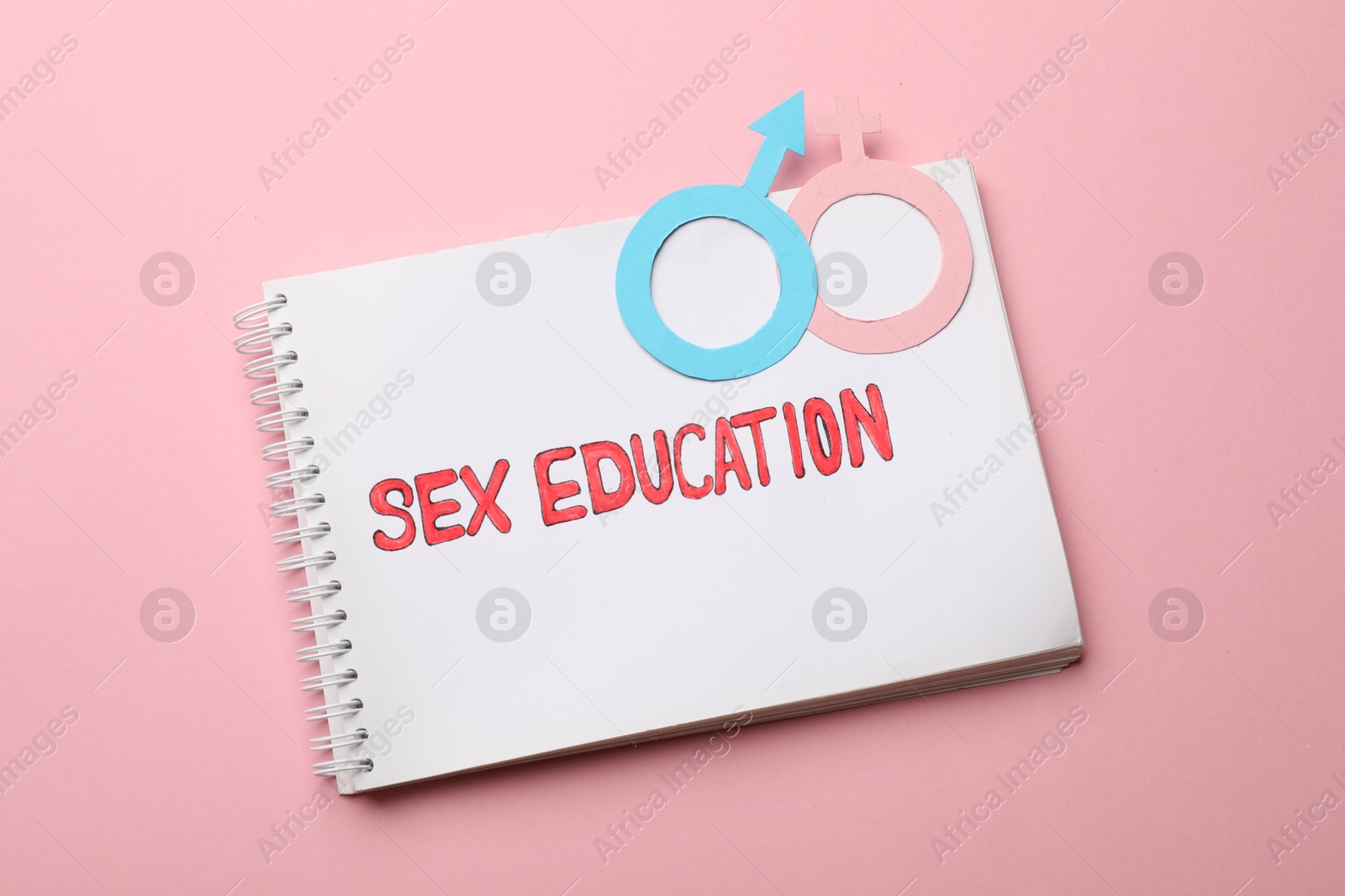 Photo of Notebook with words Sex Education and gender symbols on pink background, top view