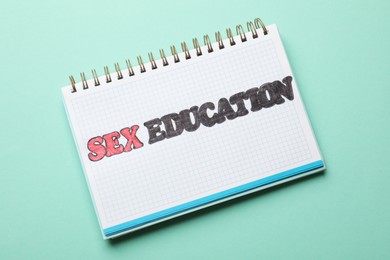 Photo of Notebook with words Sex Education on turquoise background, top view