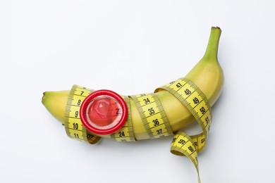 Photo of Sex education. Banana with condom and measuring tape on white background, top view