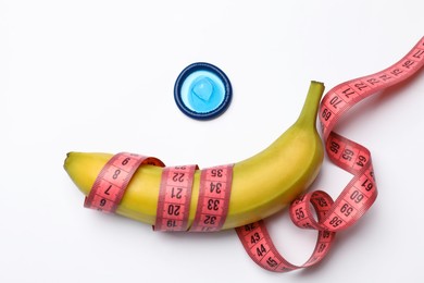 Photo of Sex education. Banana with condom and measuring tape on white background, top view
