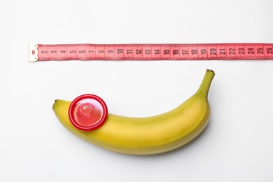 Photo of Sex education. Banana with condom and measuring tape on white background, top view
