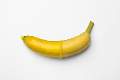 Photo of Sex education. Banana with condom on white background, top view