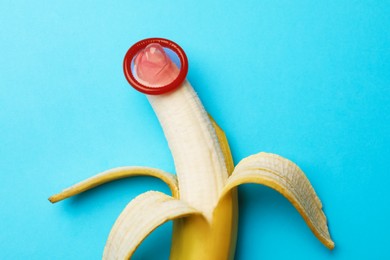 Photo of Sex education. Banana with condom on light blue background, top view