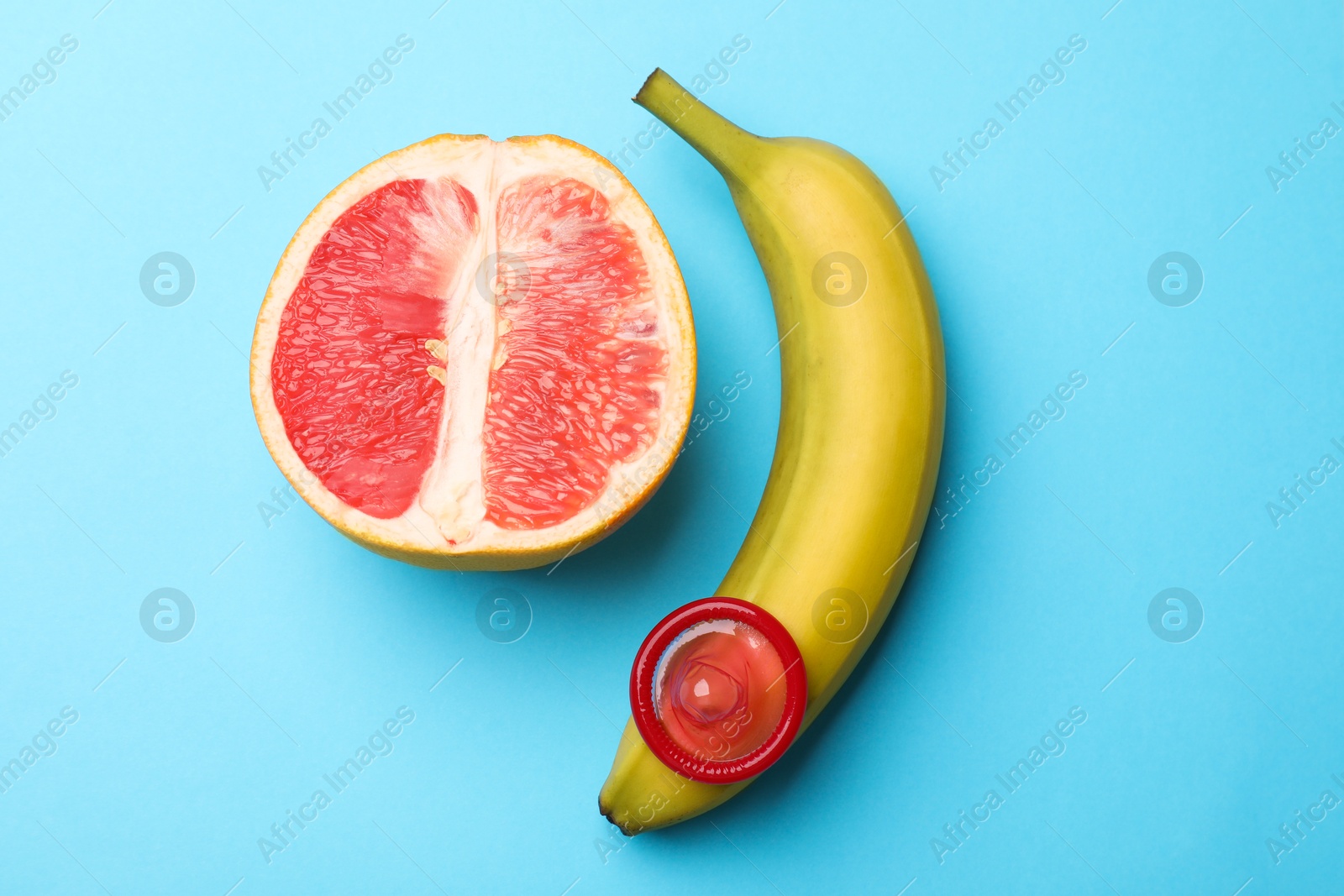 Sex education. Banana with condom and grapefruit on light blue background, top view Photo of Sex education. Banana with condom and grapefruit on light blue background, top view