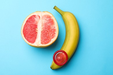 Photo of Sex education. Banana with condom and grapefruit on light blue background, top view