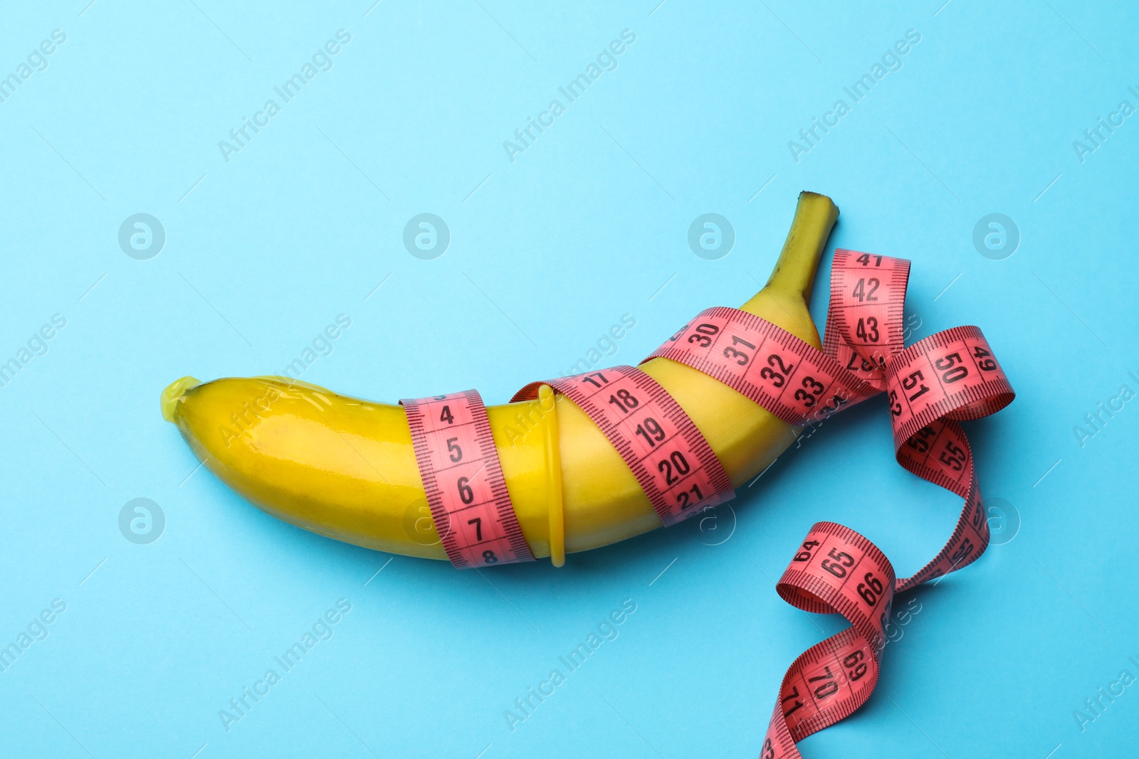 Sex education. Banana with condom and measuring tape on light blue background, top view Photo of Sex education. Banana with condom and measuring tape on light blue background, top view