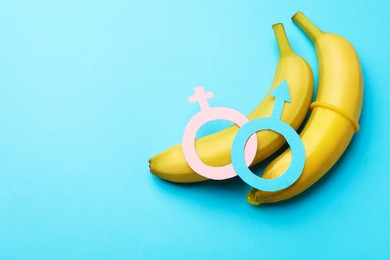 Photo of Sex education. Bananas with condom, paper female and male gender symbols on light blue background, top view. Space for text