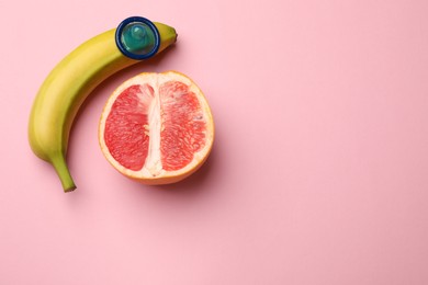 Photo of Sex education. Banana with condom and grapefruit on pink background, top view. Space for text