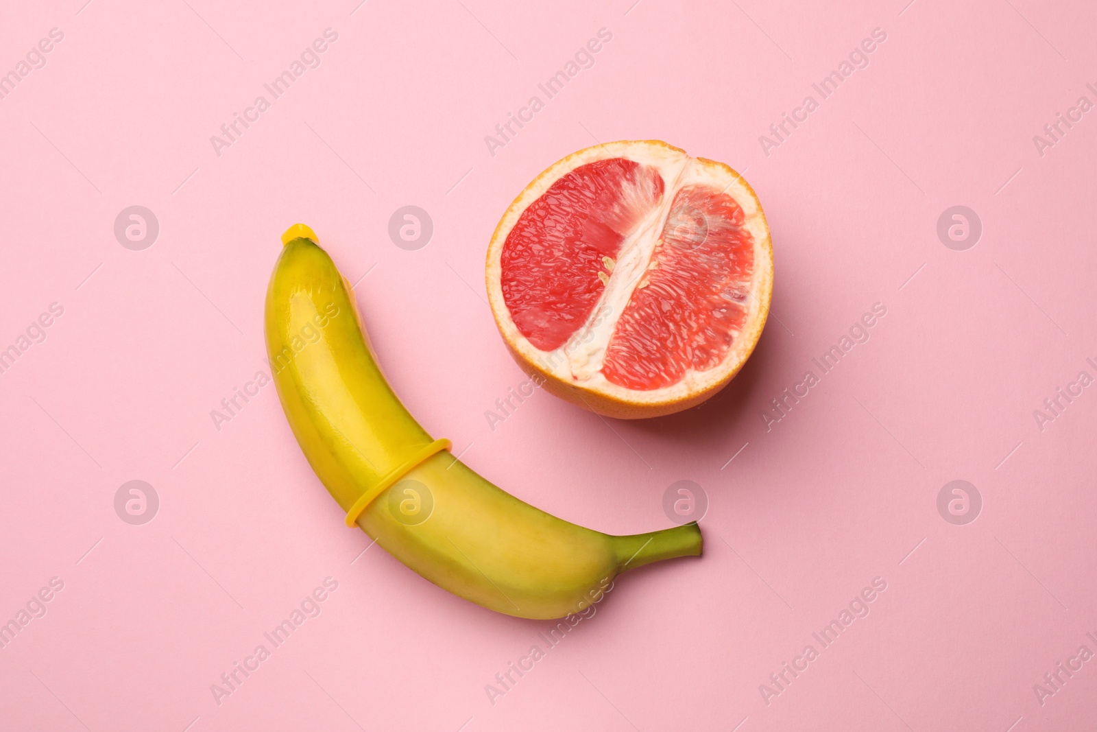 Sex education. Banana with condom and grapefruit on pink background, top view Photo of Sex education. Banana with condom and grapefruit on pink background, top view